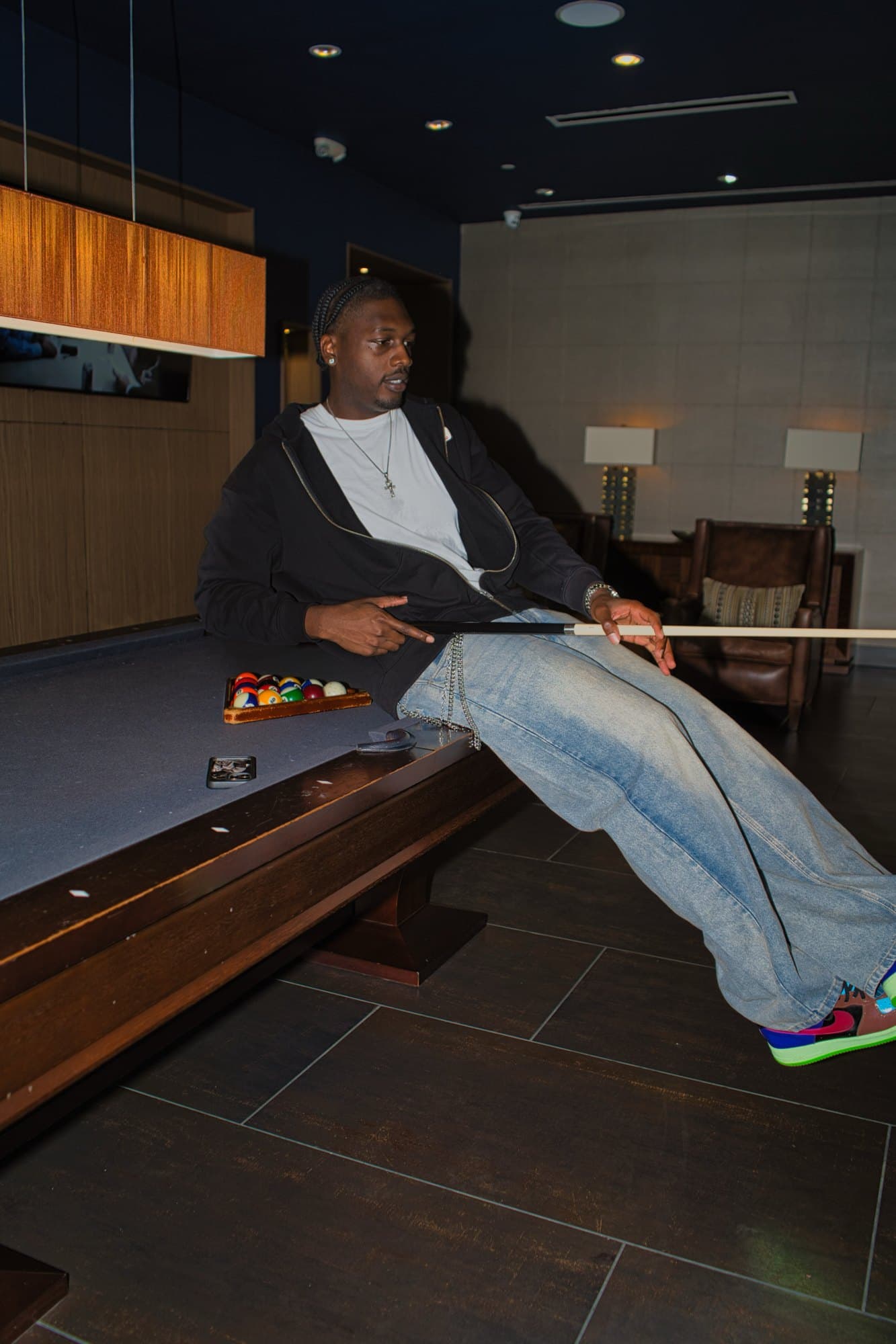 Leaning back on the pool table with a cue across the lap