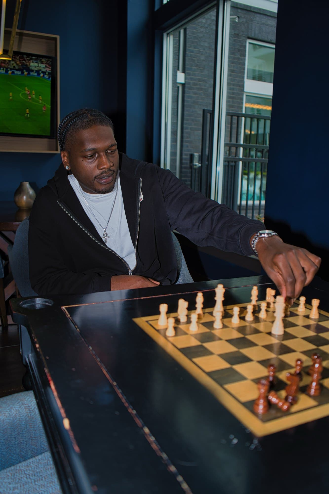 Seated portrait mid-move at a chess table in a navy lounge