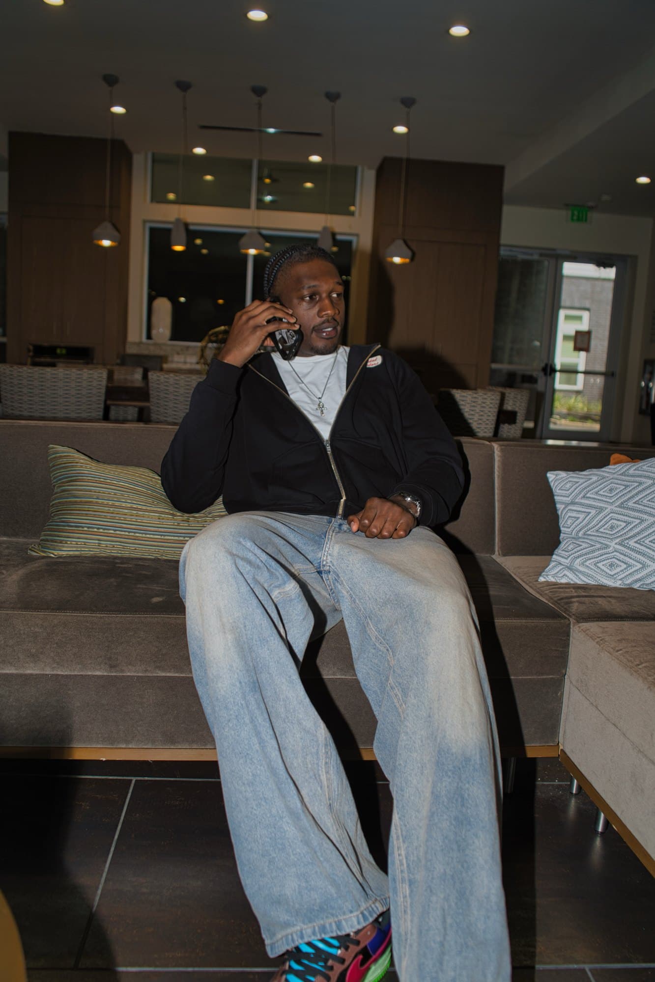 Seated on a lobby sofa taking a call under warm pendant lighting