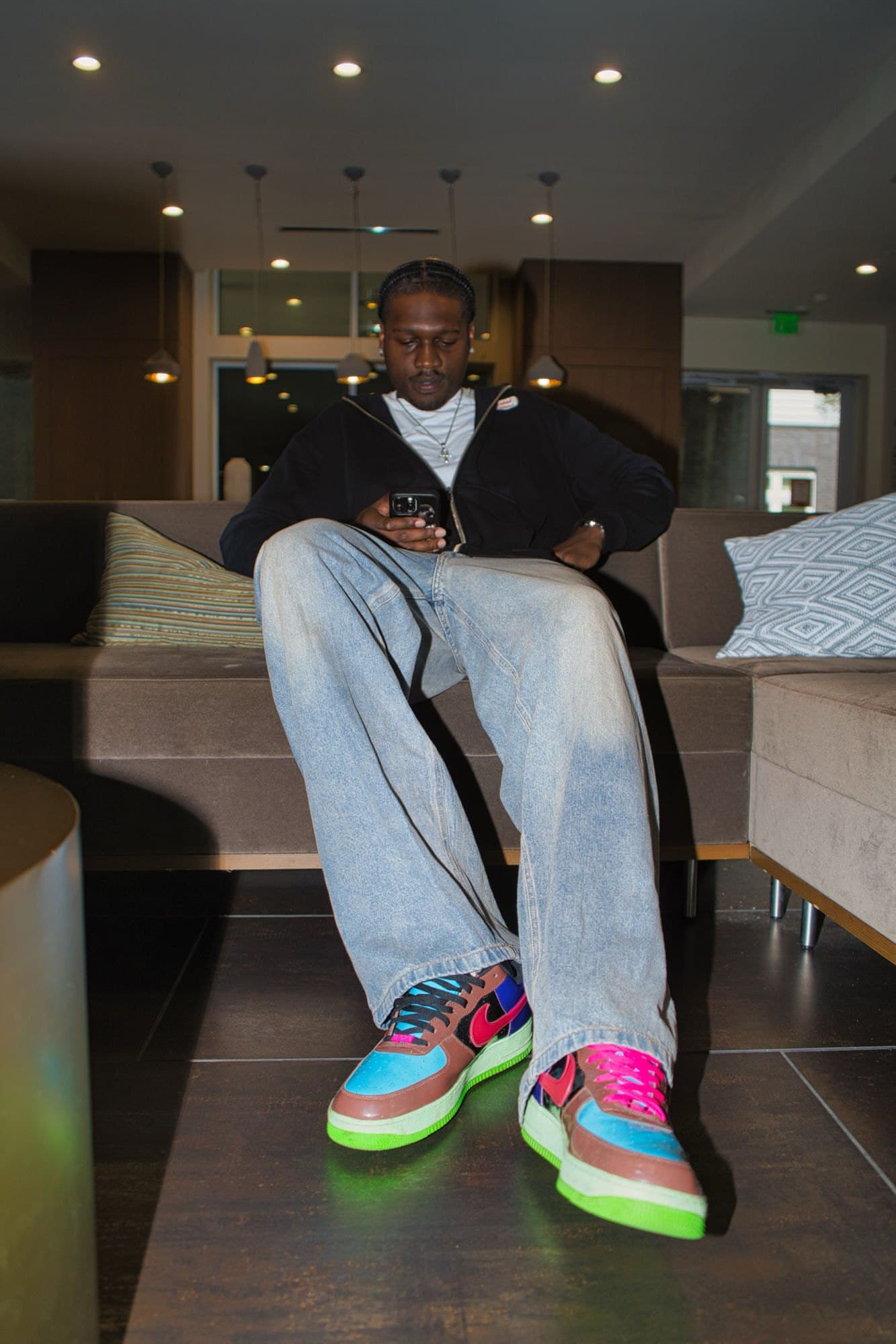 Seated portrait on a lobby sofa, wide denim and multicolour sneakers